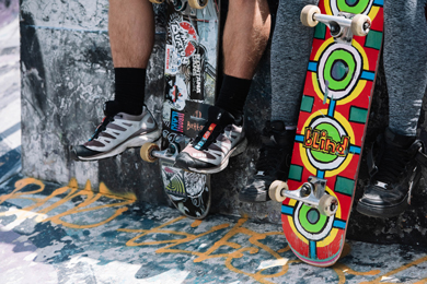 The legs of a young person sittig up on a wall v2. Two skateboards are also resting against the wall.